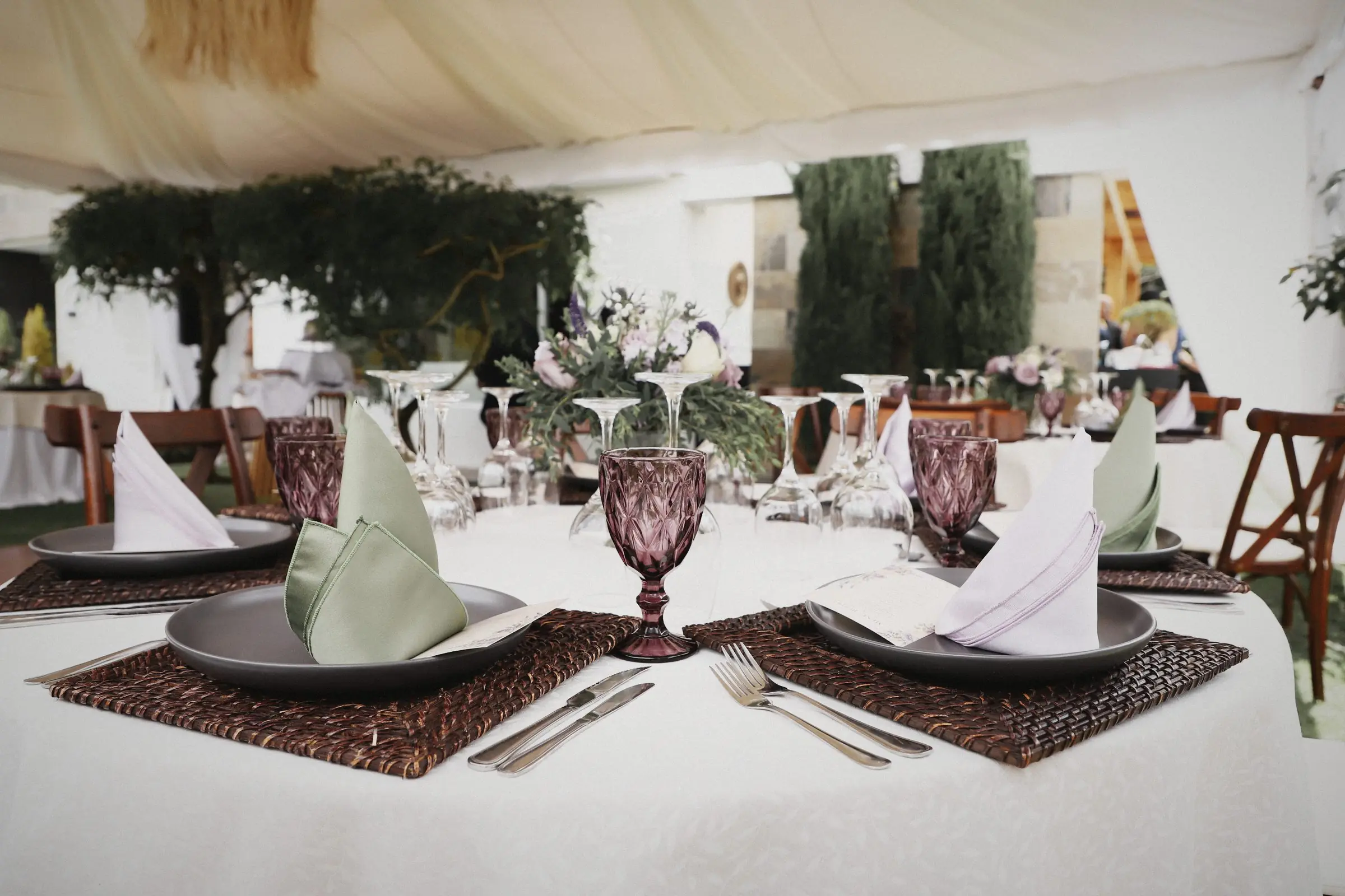 A set table: grey plates, folded linen napkins, carved glassware and woven placemats.